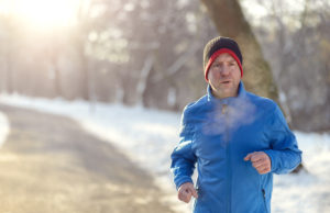 Evaluate Your Process Man out in winter weather for his daily run jogging on a paved road in a snowy landscape in a fitness and healthy lifestyle concept, close up upper body