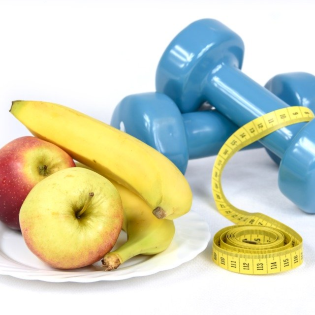 A plate of fruit next to a pair of dumbbells and a measuring tape.