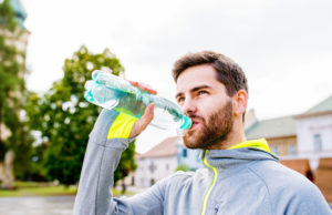 The Lake, The Beach, The Mountains & Tennis close up of young hipster runner in town with water bottle, drinking