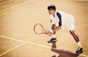 The Middle young man play tennis outdoor on orange tennis court