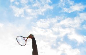 Spring Into Action Male tennis player mid-serve in silhouette with sun behind him.