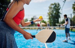Paddle Up And Ready Woman serving the ball while playing mixed doubles in pickleball.