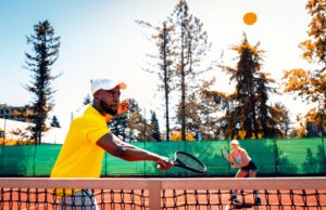 Doubles Tennis As An Exchange of Time Couple playing recreational tennis on a clay court during the day.