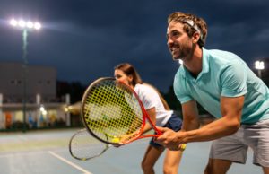 Improving Team Dynamics Tennis sport people concept. Mixed young doubles player hitting tennis ball with partner standing near net