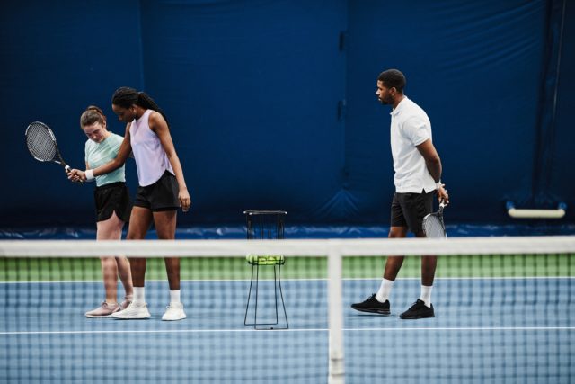 Full length portrait of female tennis coach working with young African American woman during practice at indoor court