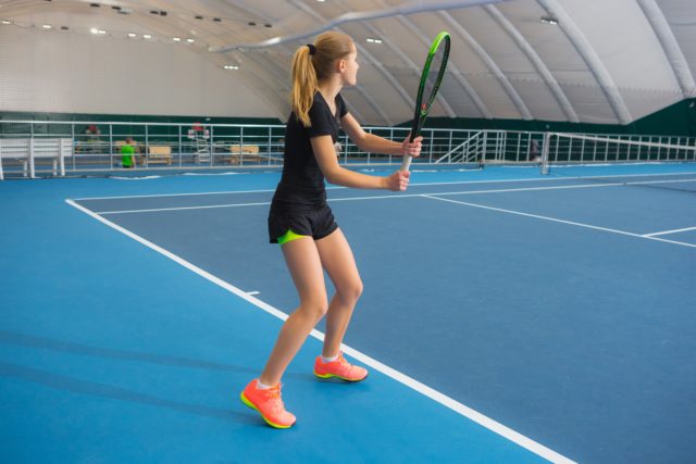 The young girl in a closed tennis court with ball and racket