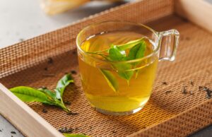 Warm Up In Cold Weather With Liquid Sport Nutrition Green tea brewed in cup with tea leaves on table. Closeup.