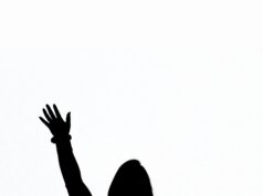 Good Question: January/February 2026 silhouette of woman standing in a crowd with hand raised as if she is asking a question.