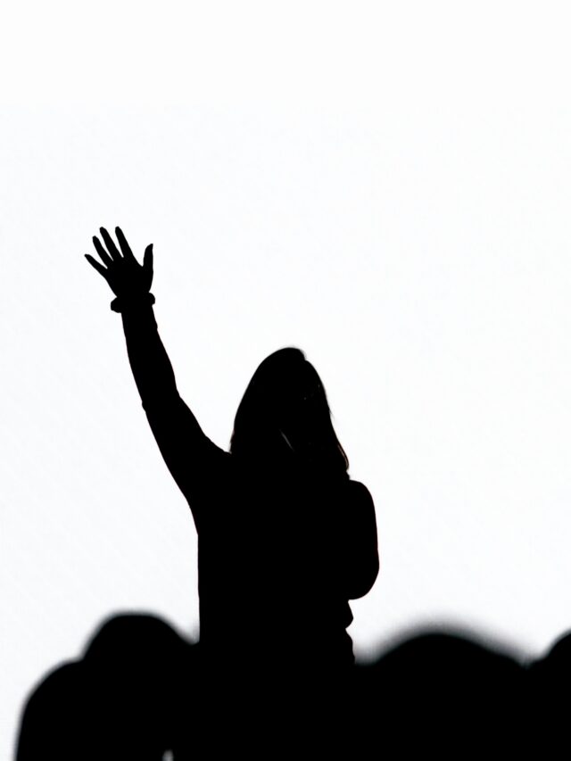 silhouette of woman standing in a crowd with hand raised as if she is asking a question.