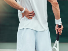 Pain While Playing? Pause Before Pushing Through Rearview unknown mixed race tennis player suffering from backache in court game. Hispanic fit athle.