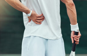Pain While Playing? Pause Before Pushing Through Rearview unknown mixed race tennis player suffering from backache in court game. Hispanic fit athle.