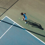 High angle view of african american female player serving during tennis game at court on sunny day. unaltered, sport, competition and tennis game concept.