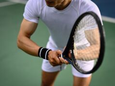 It’s Gear Time! Muscular man with racket standing in ready position to receive a serve, practicing for competition on a court.