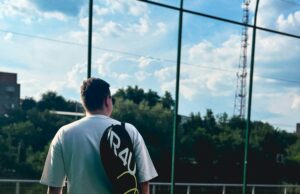 Take Back The Court Male tennis player standing on a court with a racquet bag over his shoulder.