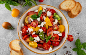 Tomato, Peach, and Burrata Salad A salad of farm fresh multi-colored tomatoes, red onion, fresh basil and feta cheese in a bowl. Summer salad. Top view