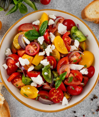 Tomato, Peach, and Burrata Salad A salad of farm fresh multi-colored tomatoes, red onion, fresh basil and feta cheese in a bowl. Summer salad. Top view