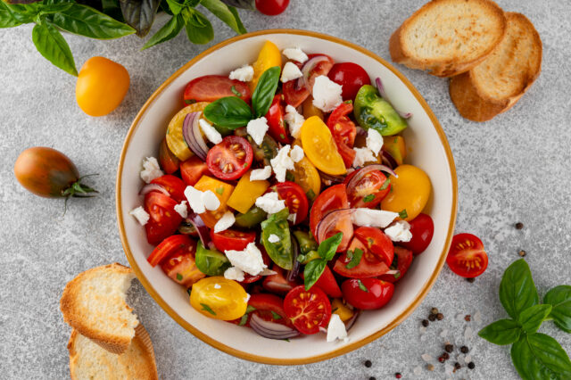 A salad of farm fresh multi-colored tomatoes, red onion, fresh basil and feta cheese in a bowl. Summer salad. Top view. A salad of farm fresh multi-colored tomatoes, red onion, fresh basil and feta cheese in a bowl. Summer salad. Top view