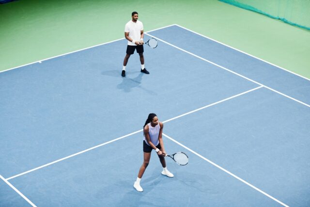 Couple at Tennis Practice Minimal Minimal high angle shot of African American couple playing tennis in pair at indoor court, copy space